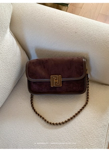 Détail du sac en daim marron foncé avec boucle dorée posé sur un canapé en tissu crème