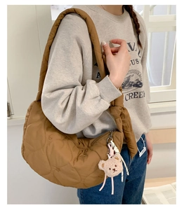 Détail d'un sac matelassé marron avec un pendentif ours en peluche et une fermeture éclair