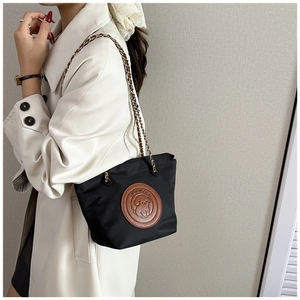 Détail du sac seau en nylon noir avec écusson en cuir et bandoulière en chaîne