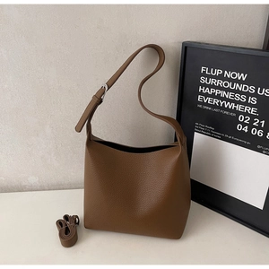 Macro detail of brown lychee grain leather texture and adjustable shoulder strap on tote bag