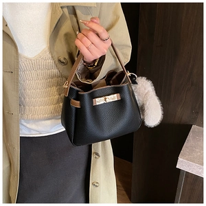 Detail of black pebbled leather bucket bag with brown handle and golden twist-lock closure