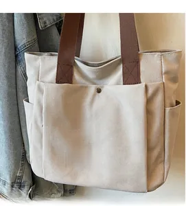Detail of beige canvas tote bag showing large front pocket with vintage metal button