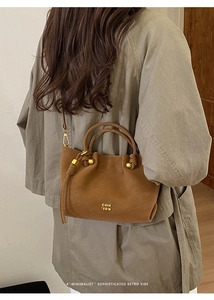 Rear view of model wearing a minimalist brown leather bucket bag with golden hardware