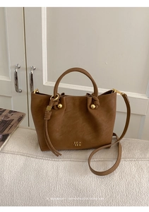 Detail of a brown leather bucket bag with gold hardware and knotted strap on a sofa
