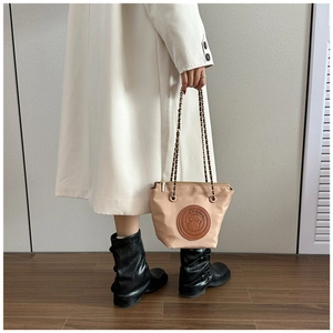 Detail of beige nylon bag with embossed dog logo and metallic chain strap worn with coat