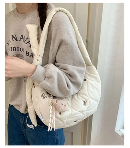 Détail d'un sac bandoulière matelassé blanc cassé avec broderie ours et breloque