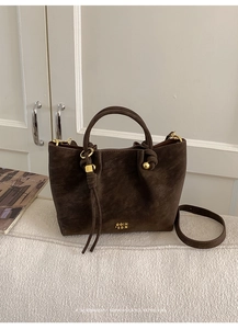 Detail of dark brown suede bucket bag with gold hardware and leather tassel on a sofa