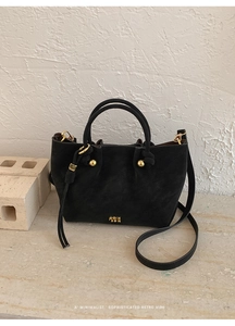 Detail of black suede bucket bag with gold hardware and adjustable shoulder strap