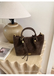 Detail of dark brown suede bucket bag with knotted handle and gold logo in a warm retro setting