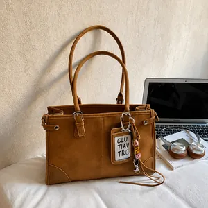Detail of caramel brown tote bag with metal buckles and hanging card holder on a desk