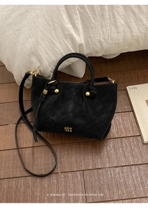 Detail of black suede bucket bag with gold hardware and brand logo on a wooden surface