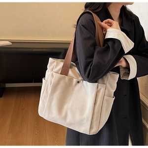 Close-up of a cream canvas tote bag with brown straps and functional metal snap button