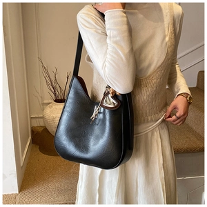 Detail of black pleated faux leather hobo bag with a decorative heart metal charm