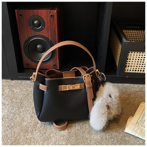 Detail of black lychee grain bucket bag with gold square lock and a plush bunny charm