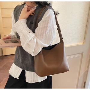 Detail of a brown lychee pattern leather shoulder bag worn by a model in a soft setting