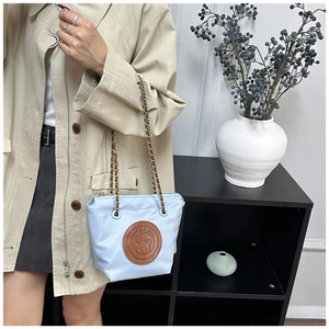 Close-up of light blue chain bag with round brown leather patch and dog illustration