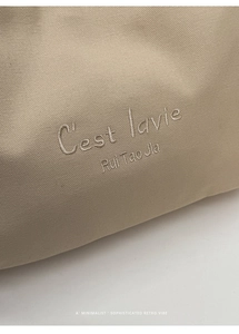 Macro detail of beige canvas tote featuring intricate C'est lavie embroidery and texture