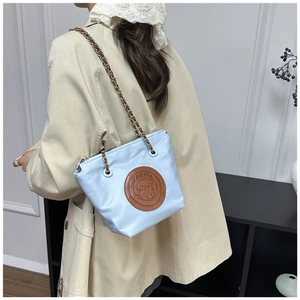 Détail du sac cabas en nylon bleu clair avec écusson en cuir et bandoulière chaîne