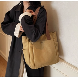 Detail of khaki canvas tote bag with brown straps and large front pocket on a model