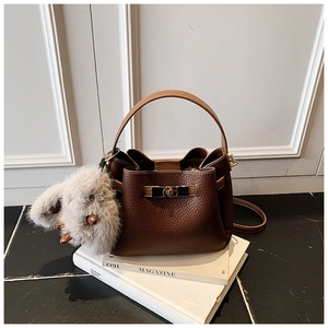 Detail of dark brown pebble leather bucket bag with metallic buckle and plush rabbit charm