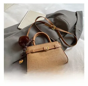 Detail view of brown woven crossbody bucket bag with gold buckle and faux fur pompom charm