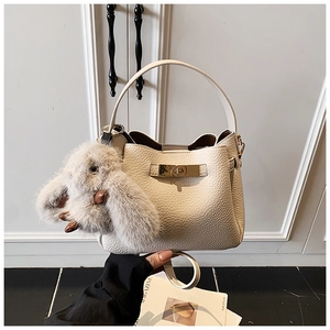 Detail view of beige lychee leather bucket bag with gold lock and rabbit pendant