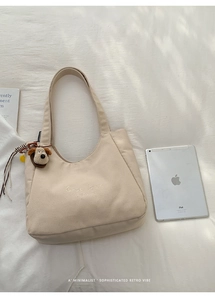 Detail view of beige canvas tote bag with embroidery text and cute plush dog charm