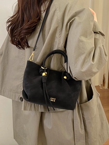 Chic black matte bucket bag with gold hardware and drawstring, styled with a trench coat