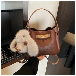 Close-up of brown litchi grain leather bucket bag with gold clasp and plush rabbit charm