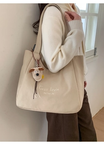 Detail of a beige canvas tote bag with embroidery and a plush puppy charm on a wide strap