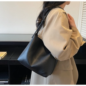 Macro detail of black litchi grain leather tote with adjustable shoulder strap on model