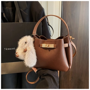 Detail of brown litchi pattern bucket bag with gold twist lock and plush rabbit charm