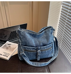 Close-up of washed blue denim crossbody bag with multiple zippers and metal buckles