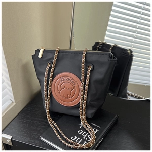 Detail of black nylon tote bag featuring brown cartoon dog patch and gold chain strap