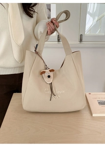 Detail of cream canvas tote bag with embroidery and plush dog charm on wooden table