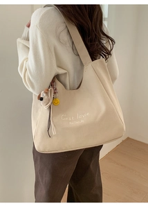 Detail of beige canvas tote bag featuring C'est lavie print and cute puppy bag charms