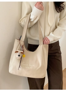 Detail of beige canvas tote bag with embroidery, cute plush puppy and smiley face charms