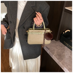 Detail of olive green woven bucket bag featuring golden buckle and brown pompom charm