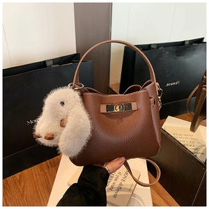 Close-up of brown litchi grain leather bucket bag with a plush white rabbit charm
