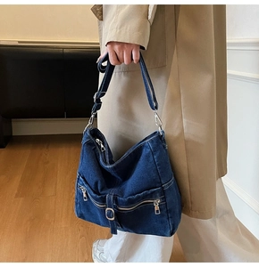 Detail of dark blue denim crossbody bag featuring functional zippers and adjustable strap