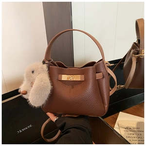 Close-up of brown litchi pattern leather bucket bag with golden buckle and rabbit charm