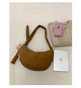 Détail d'un sac demi-lune matelassé marron avec pendentif ours sur tissu doux