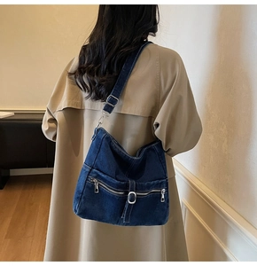 Detail of dark blue denim hobo bag with silver zipper and metal buckle on trench coat