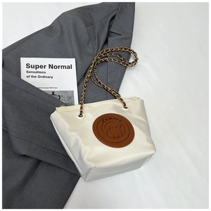 Close-up of beige tote bag with brown cartoon dog patch and chain strap detail