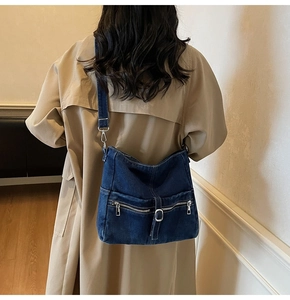 Fashionable denim tote bag worn over the shoulder by a model in a beige trench coat