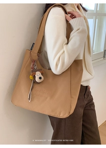 Detail of camel canvas tote bag with 'C'est la vie' embroidery and a cute puppy plush charm