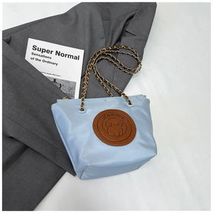 Detail of light blue nylon bag with a brown puppy leather patch and gold chain strap