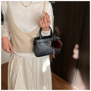 Close-up of black woven texture handbag with gold buckle and plush ball charm accessory