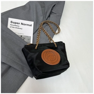 Detail of black satin bag with vintage brown leather patch and gold chain strap