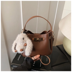 Detail of dark brown litchi textured bucket bag with a plush bunny charm on books